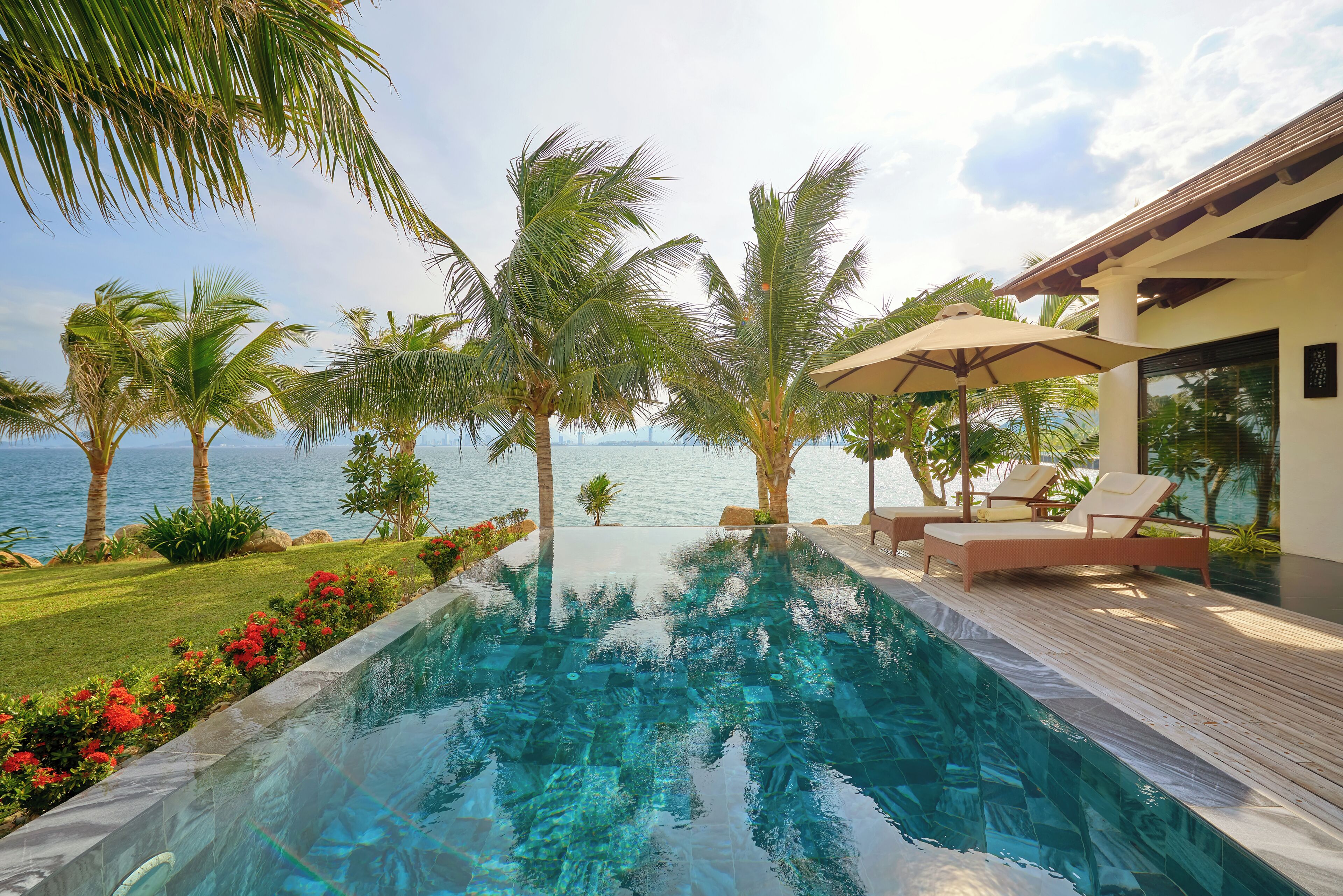 A swimming pool with a wooden deck, lounge chairs, and palm trees.