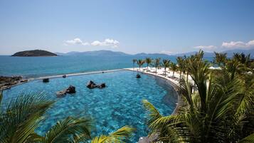 A clear blue pool with rocks, surrounded by palm trees and a beach area.