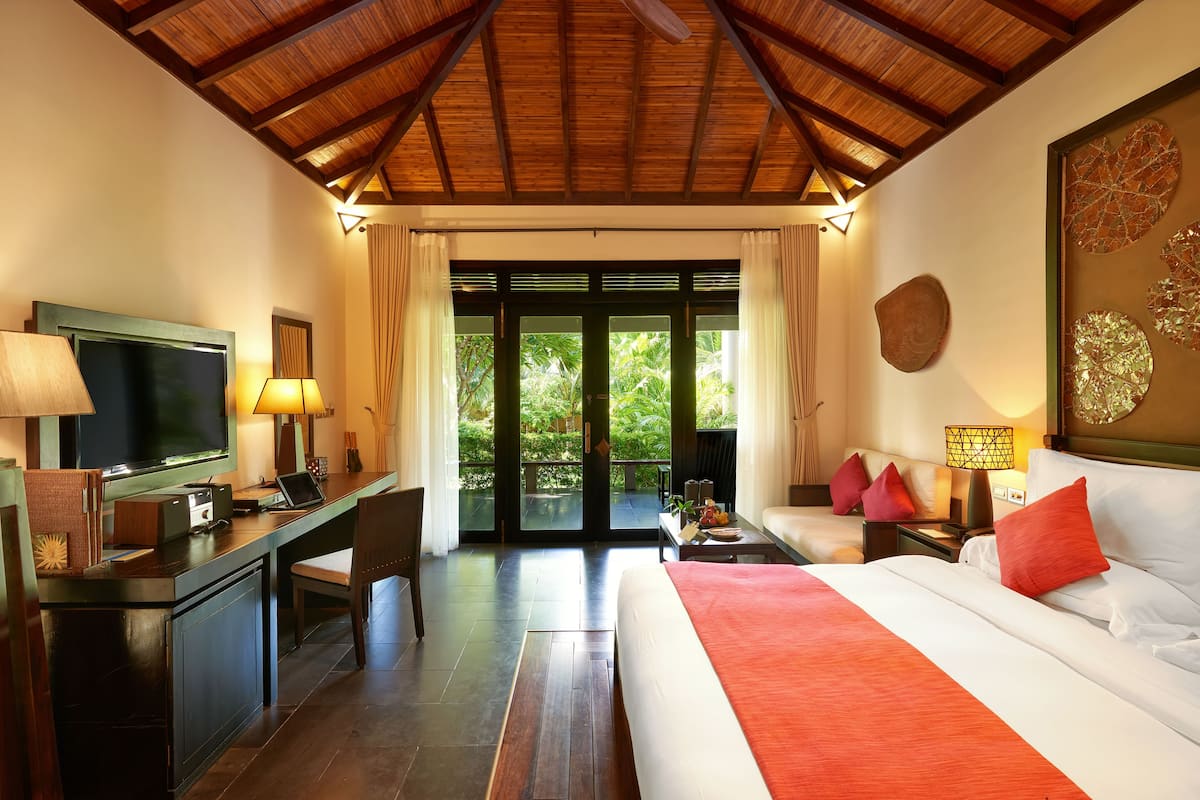 Une chambre d’hôtel avec un grand lit, un bureau avec un ordinateur, une télévision et un balcon donnant sur un paysage verdoyant.