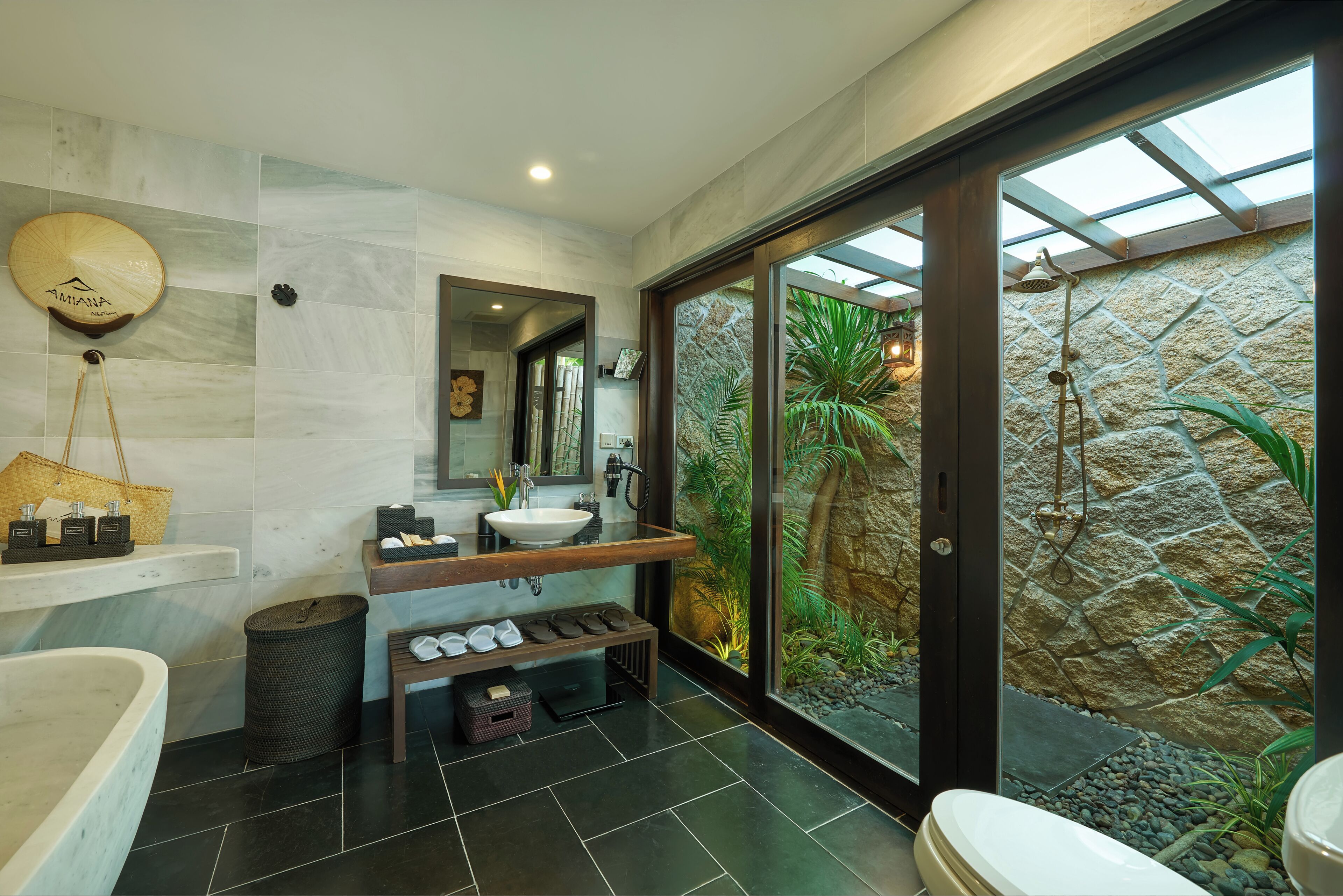 A modern bathroom with a large bathtub, a vanity with a mirror, and a stone wall with a view of greenery.