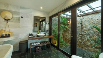A modern bathroom with a large bathtub, a vanity with a mirror, and a stone wall with a view of greenery.
