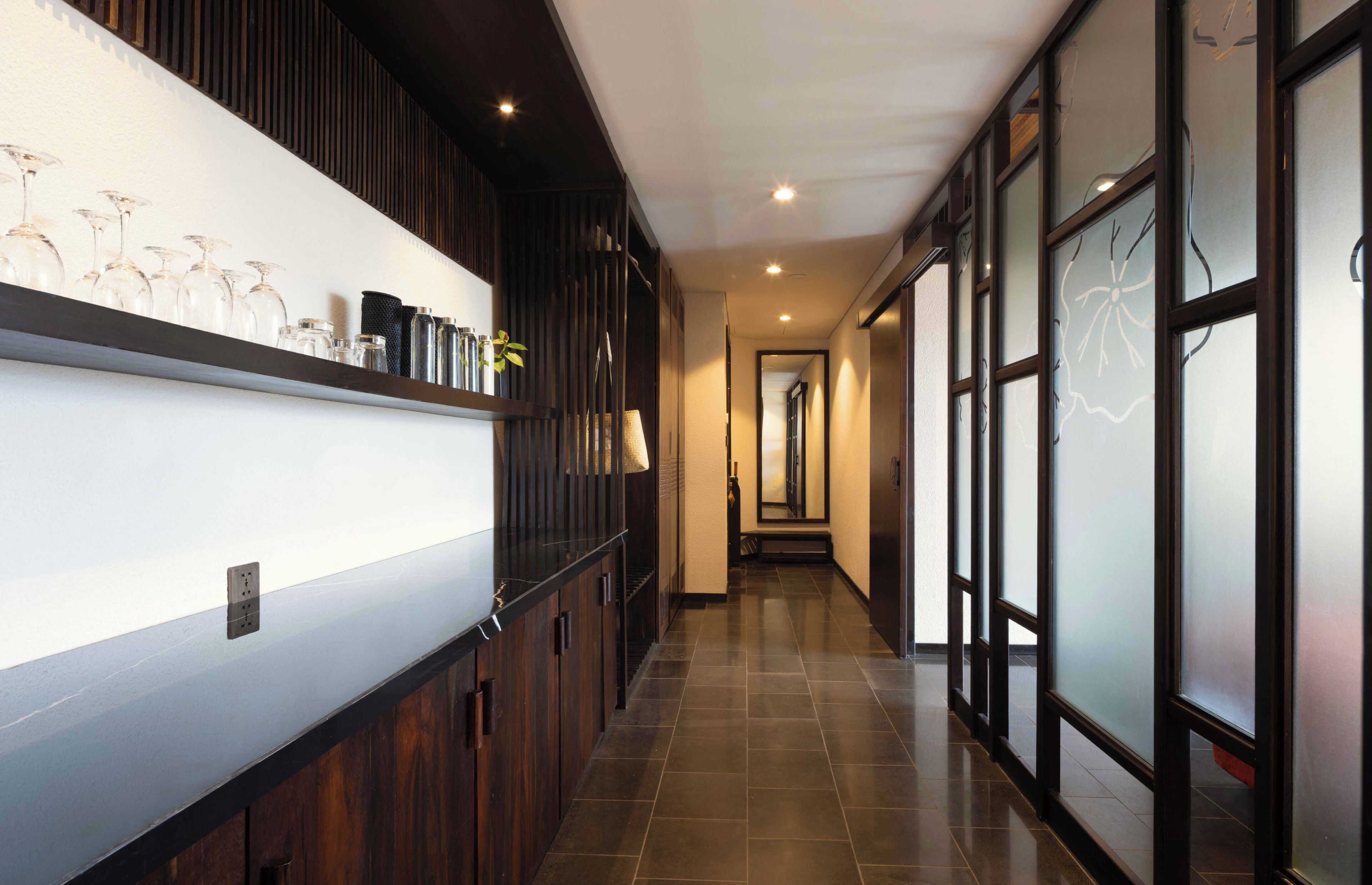 A hallway with a wooden wall, a shelf with glassware, and a tiled floor.