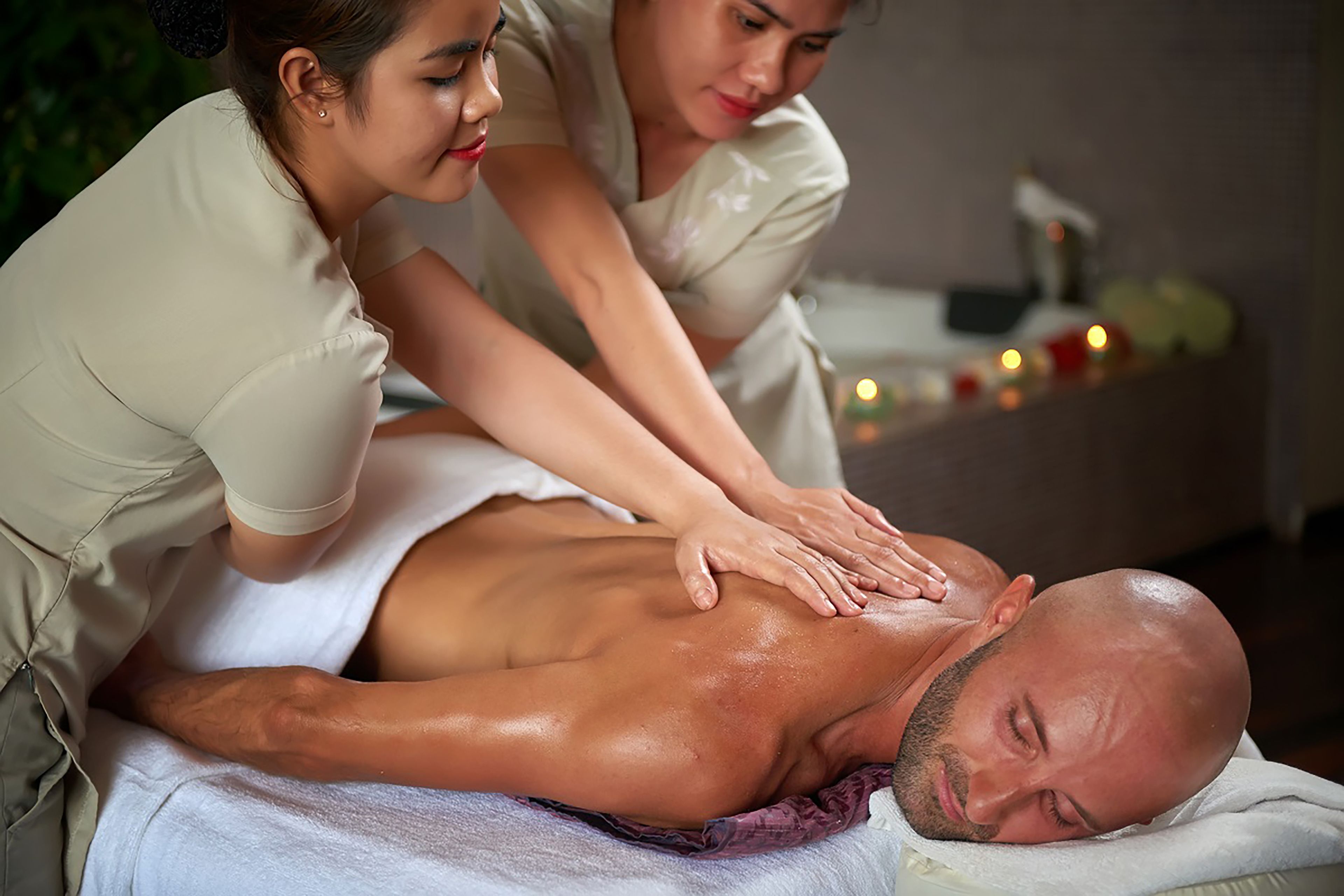 A massage therapy session in a spa setting with a client lying face down on a massage table, a therapist attending to the client, and a small table with candles in the background.