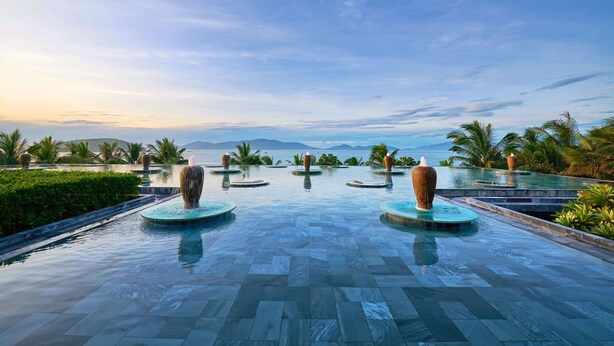 A serene infinity pool with decorative vases, surrounded by lush greenery and palm trees, overlooking a scenic view of the ocean and distant mountains. - Amiana Resort Nha Trang (Bac Nha Trang)