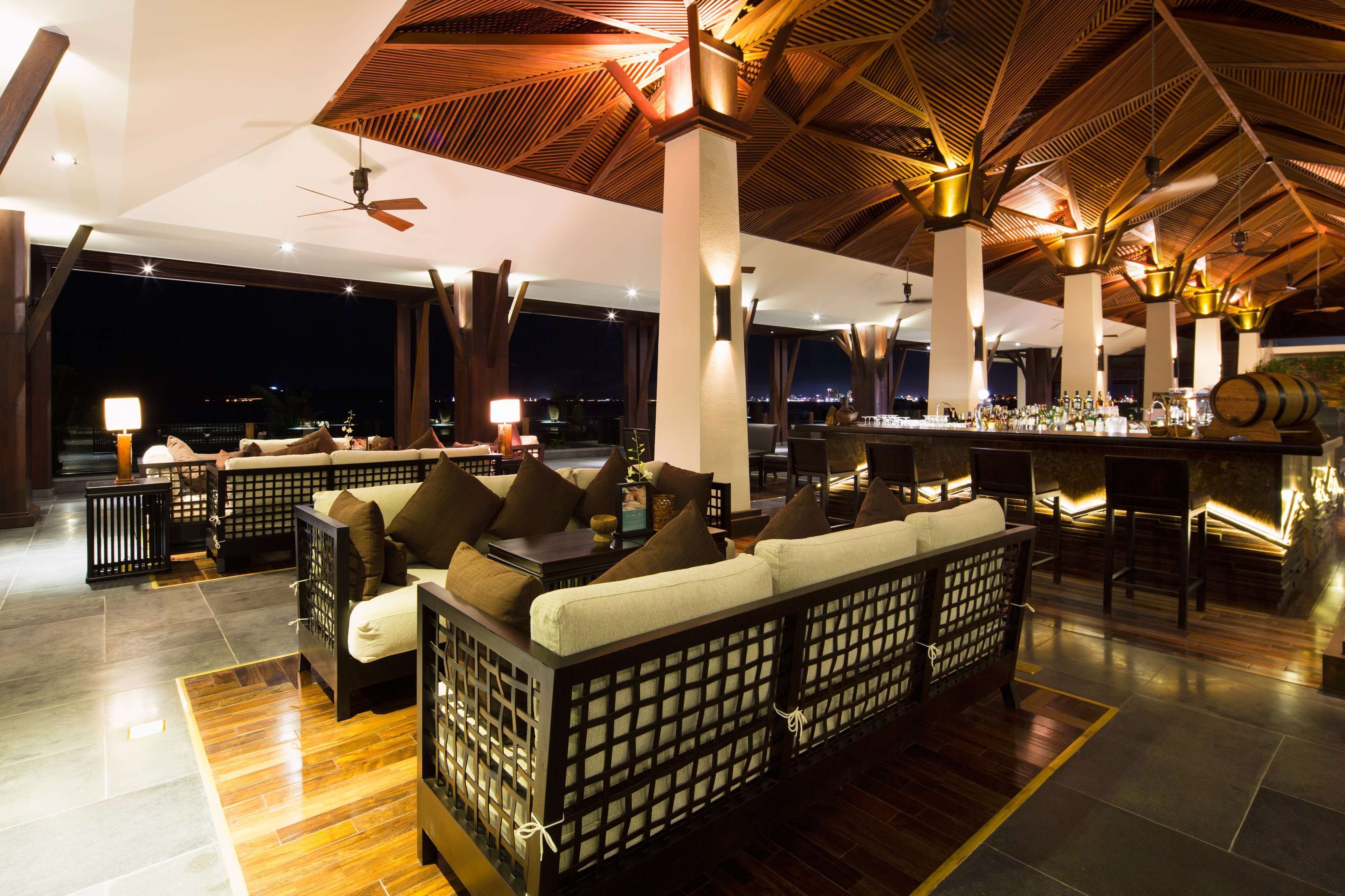 A spacious lounge area with a high ceiling, wooden beams, and a bar with a view of the city at night.