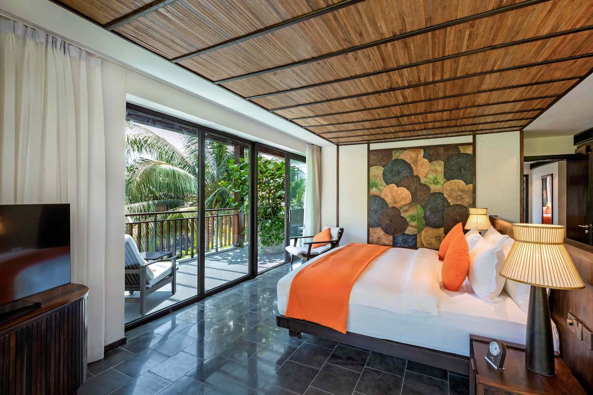 Une chambre spacieuse avec un grand lit, une télévision et un balcon doté d’un coin salon extérieur.