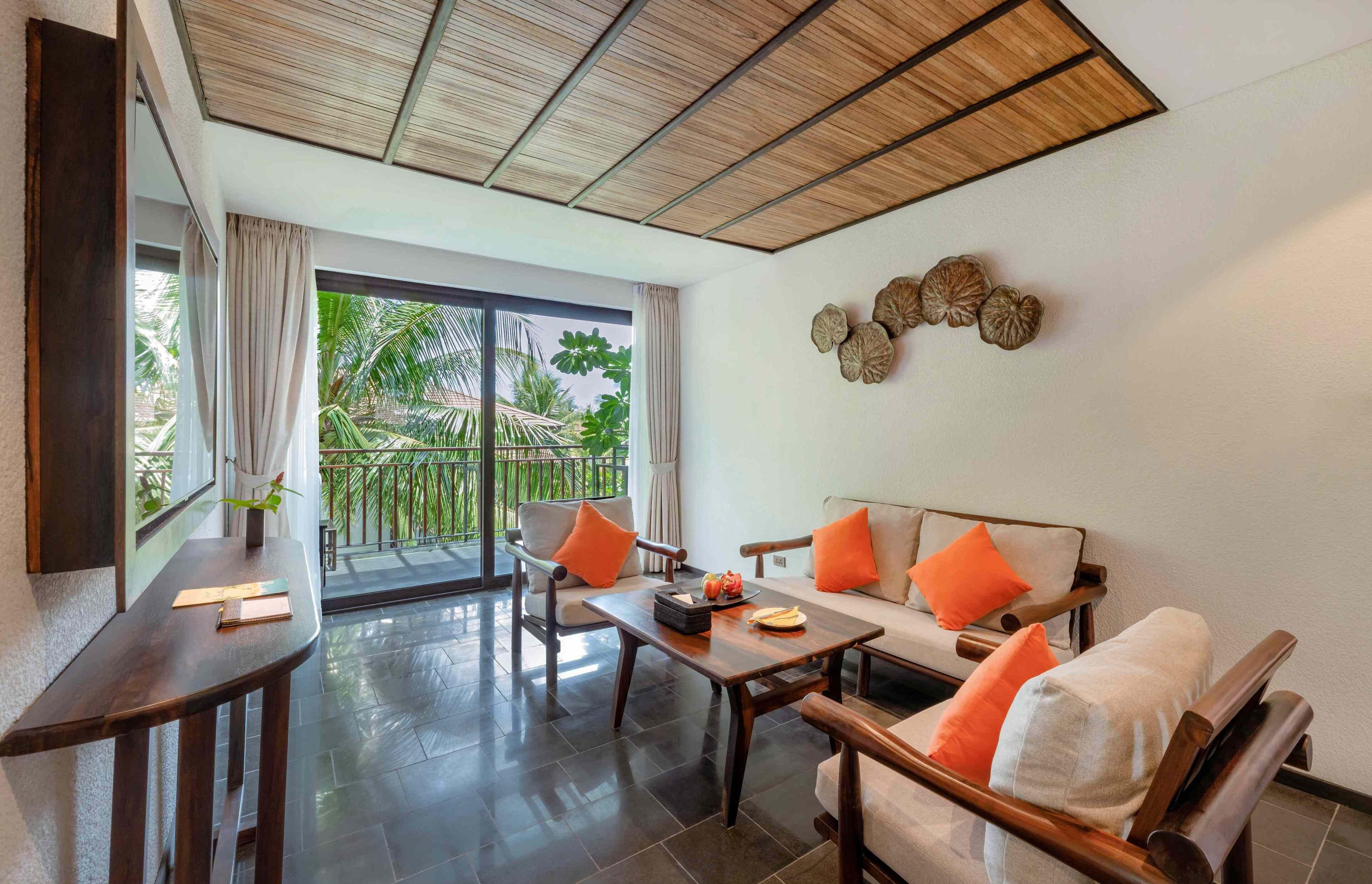 Ein modernes Zimmer mit einer Couch, Stühlen, einem Tisch und einem Balkon mit Blick auf Grünfläche.