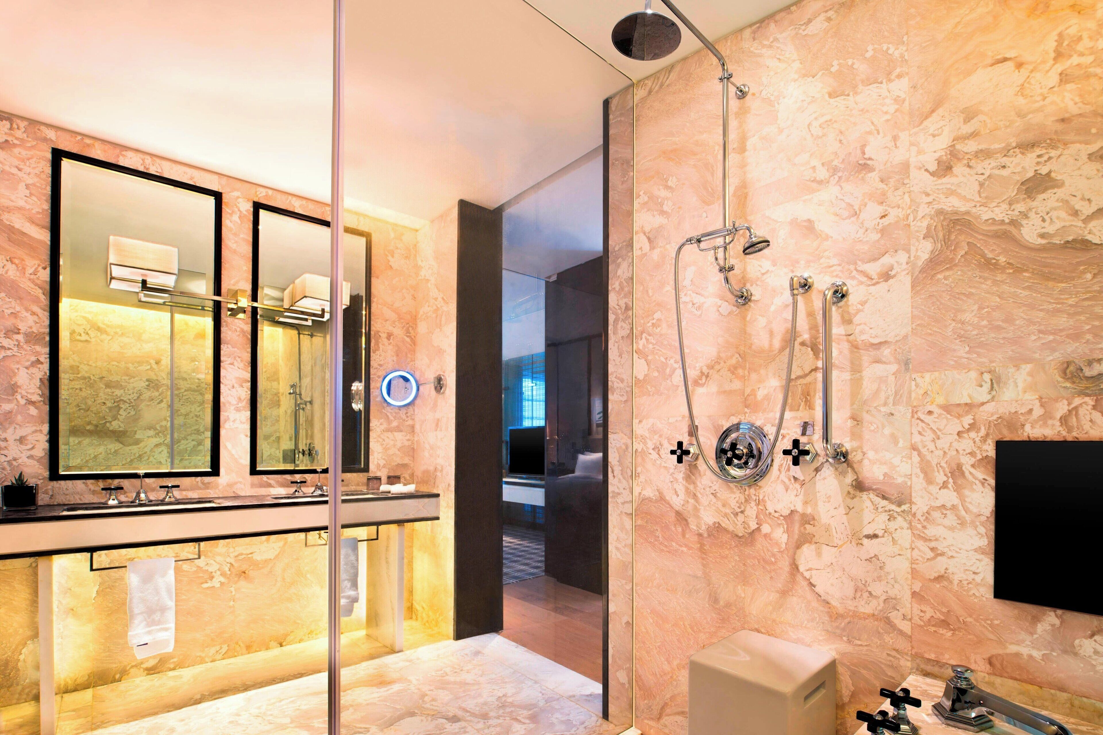 Ein modernes Badezimmer mit einer Glaskabine zur Dusche, einem Waschtisch mit Spiegel und Marmorwänden.