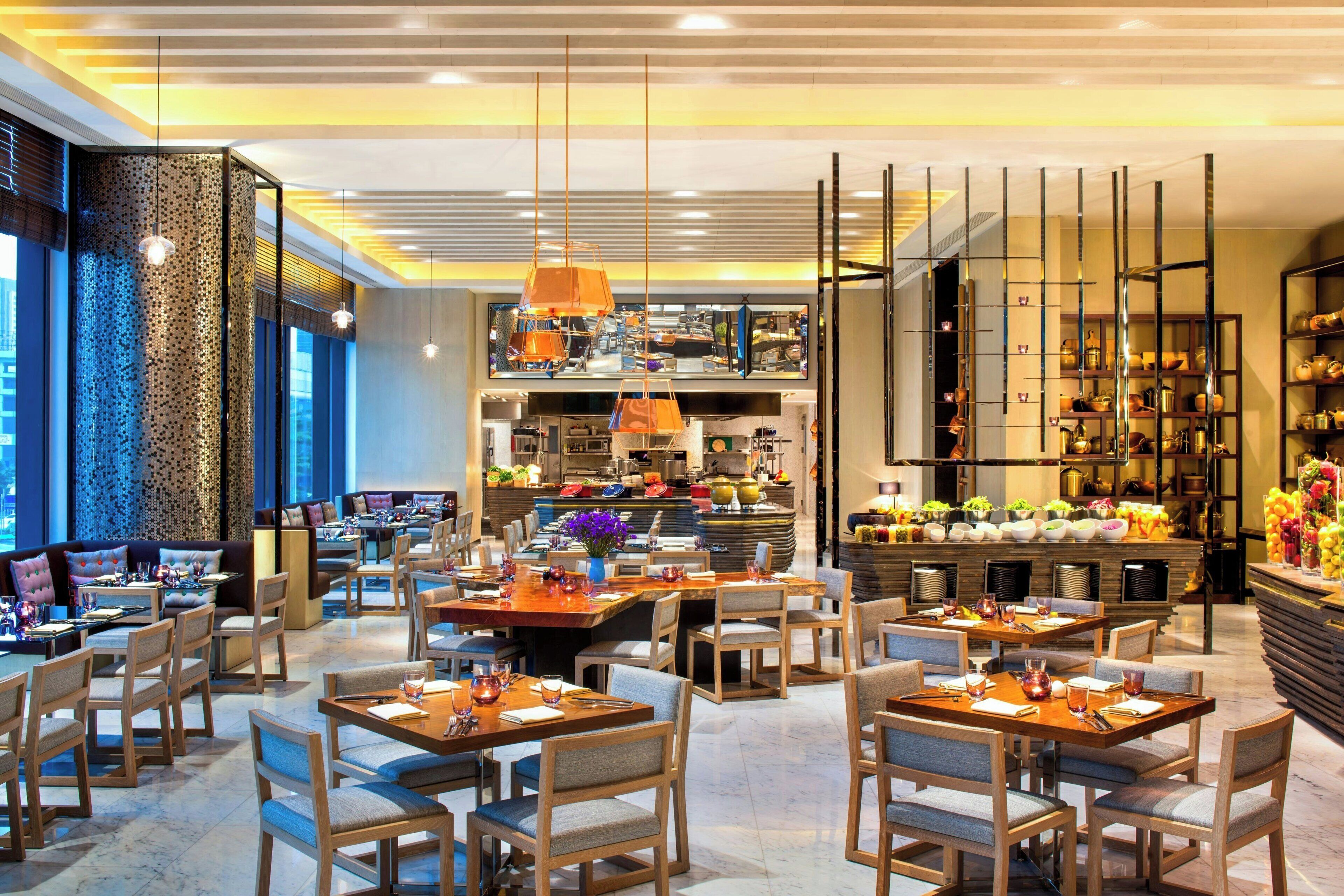 A modern restaurant with multiple dining areas, a bar, and a kitchen visible in the background.