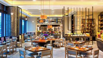 A modern restaurant with multiple dining areas, a bar, and a kitchen visible in the background.