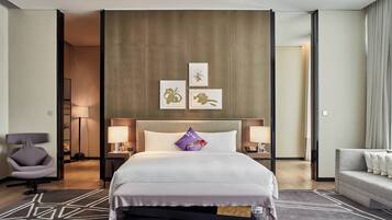 Una habitación de hotel moderna con una cama grande, dos mesitas de noche, una silla, un sofá y obras de arte en la pared.