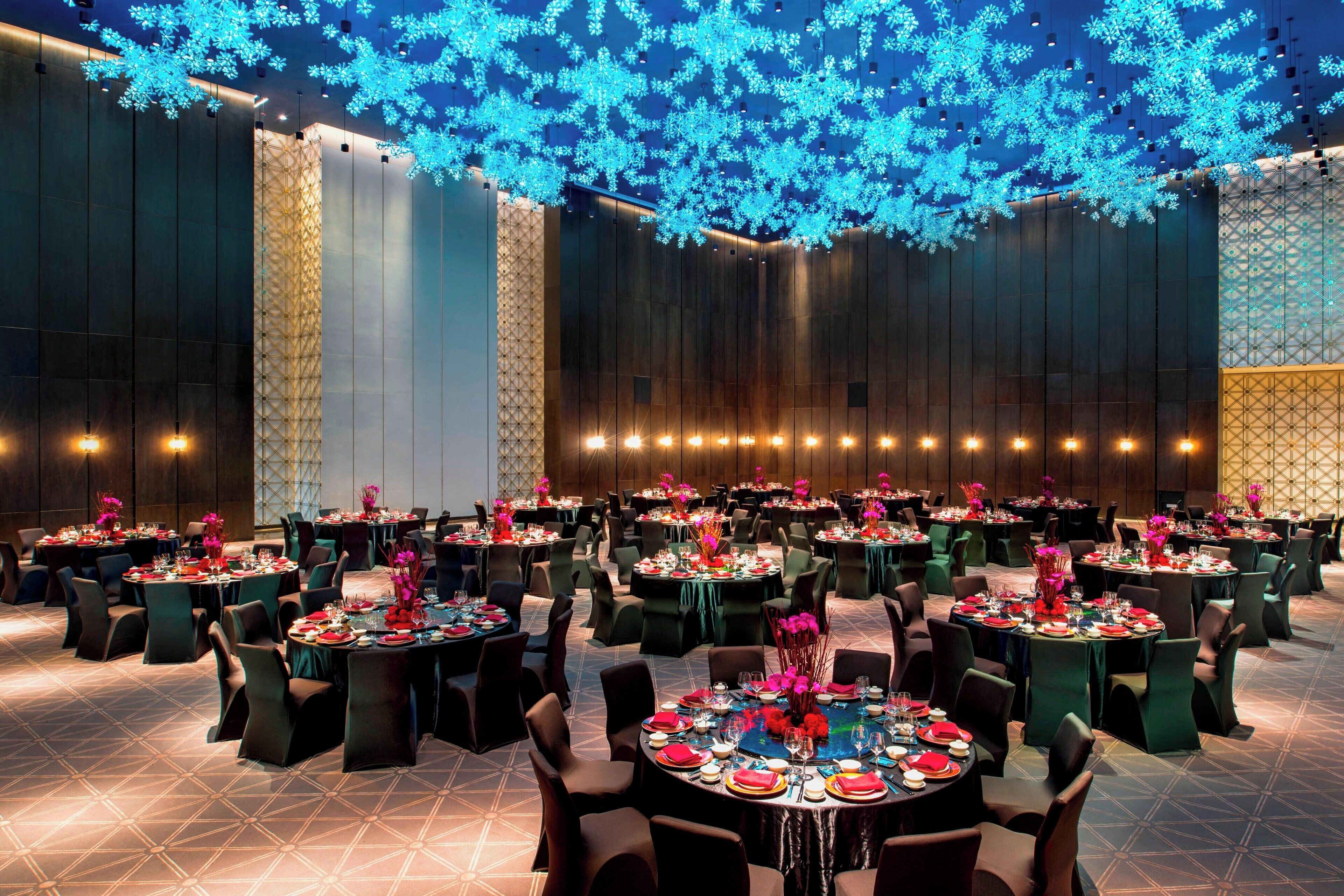 Une vaste salle de banquet, avec des tables rondes dressées pour le repas, un motif géométrique sur le sol et un plafond illuminé de jeux de lumière bleus.