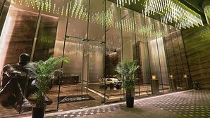 Un moderno vestíbulo de hotel con paredes de vidrio reflectante, una zona de estar central e iluminación decorativa.