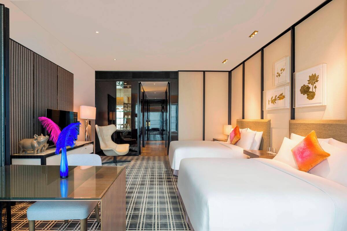 Une chambre d’hôtel avec deux lits, un bureau avec une lampe, une chaise et une sculpture décorative.