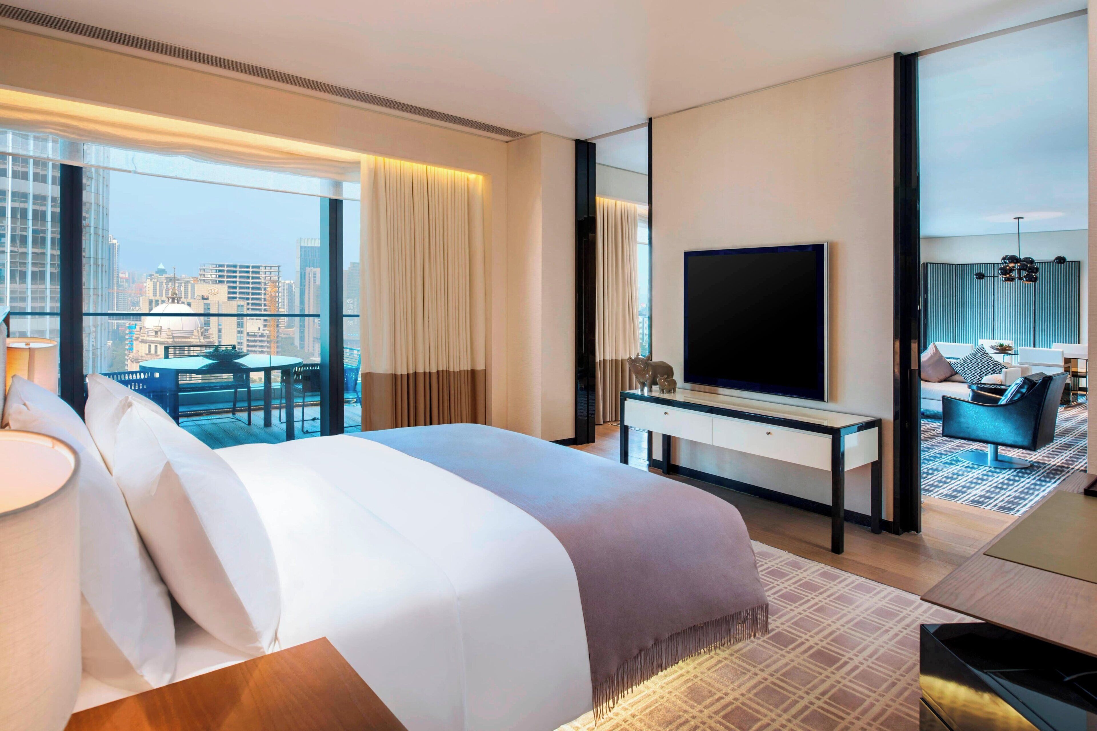 Une chambre d’hôtel avec un grand lit, une télévision, un bureau et un balcon offrant une vue sur la ville.