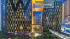 Un edificio moderno de gran altura con una fachada geométrica llamativa, ventanas amplias y un área de entrada destacada.