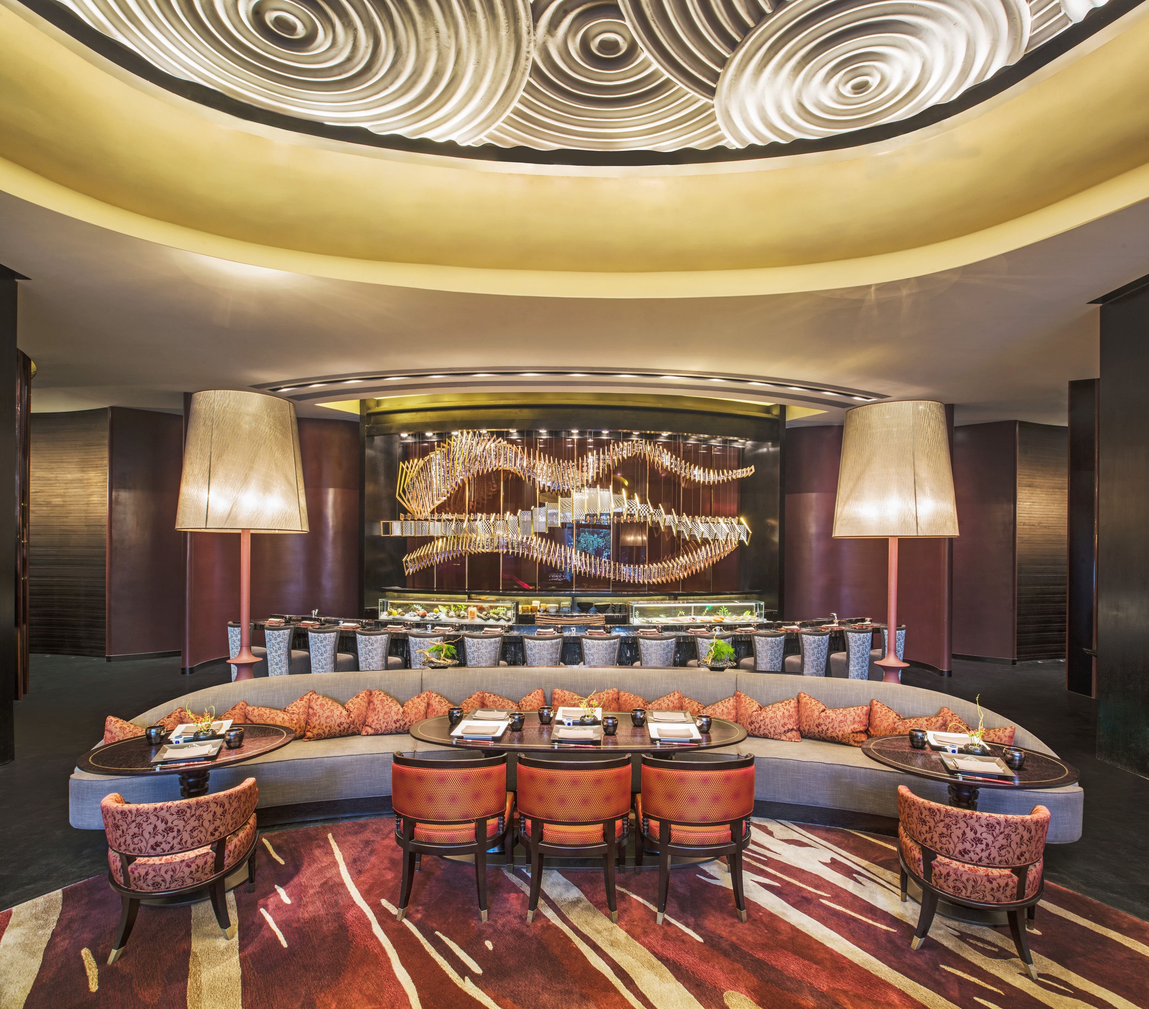 Un moderno vestíbulo de hotel con una zona de estar circular, un bar y un techo decorativo.