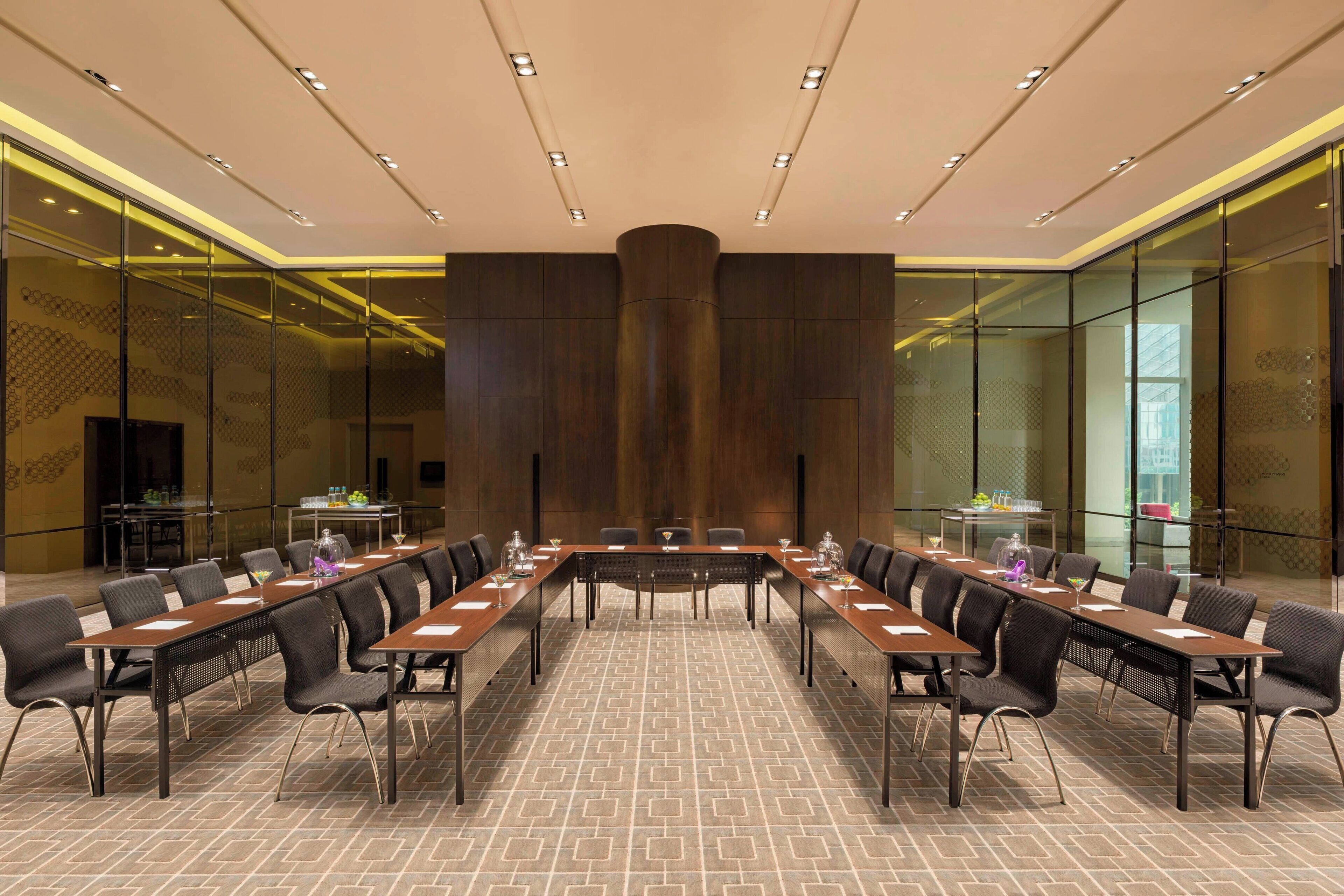 A conference room with a long table, multiple chairs, and a high ceiling with recessed lighting.
