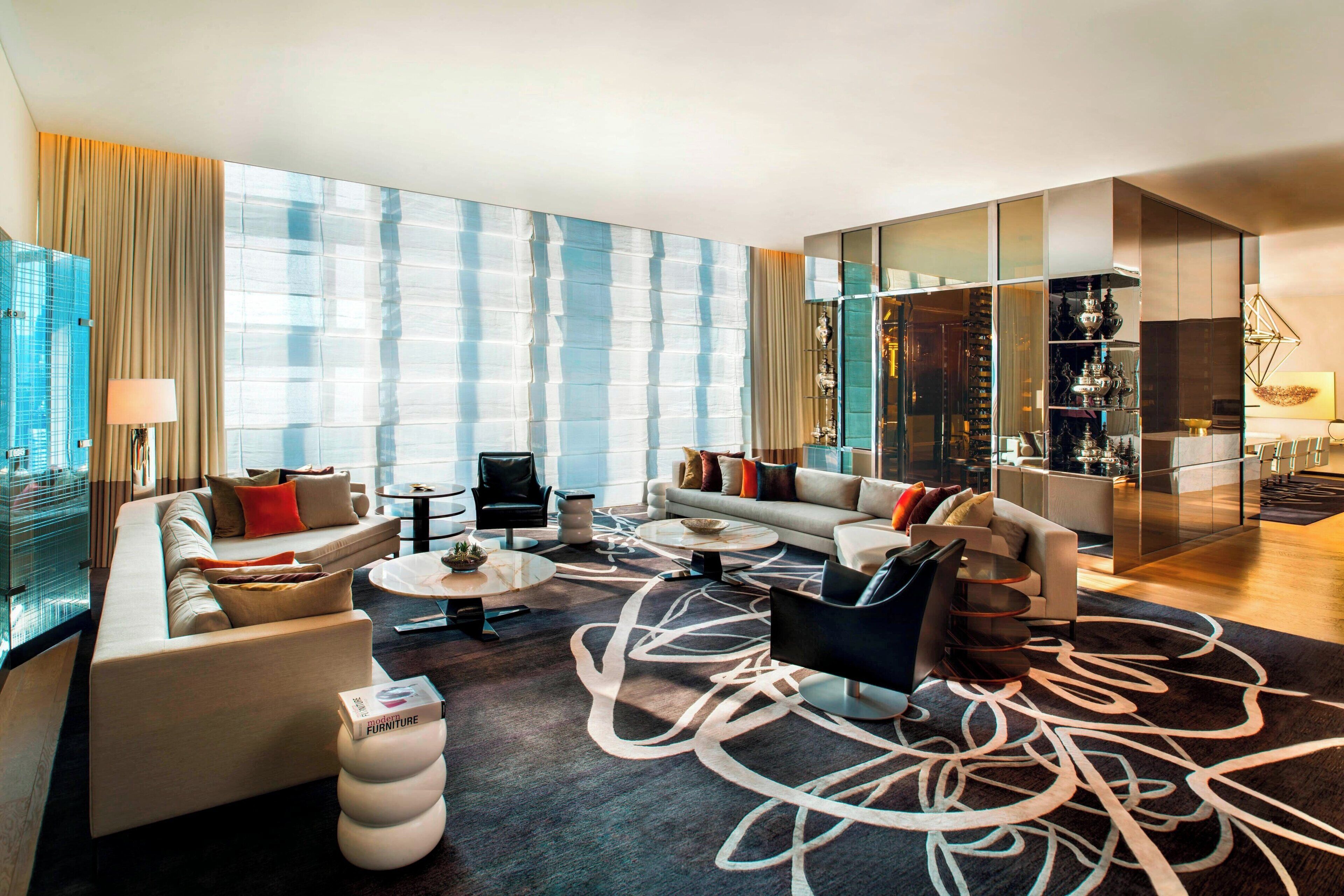 Una sala de estar moderna con un ventanal grande, un conjunto de sofás, una mesa de centro y un aparador de vidrio con objetos decorativos.