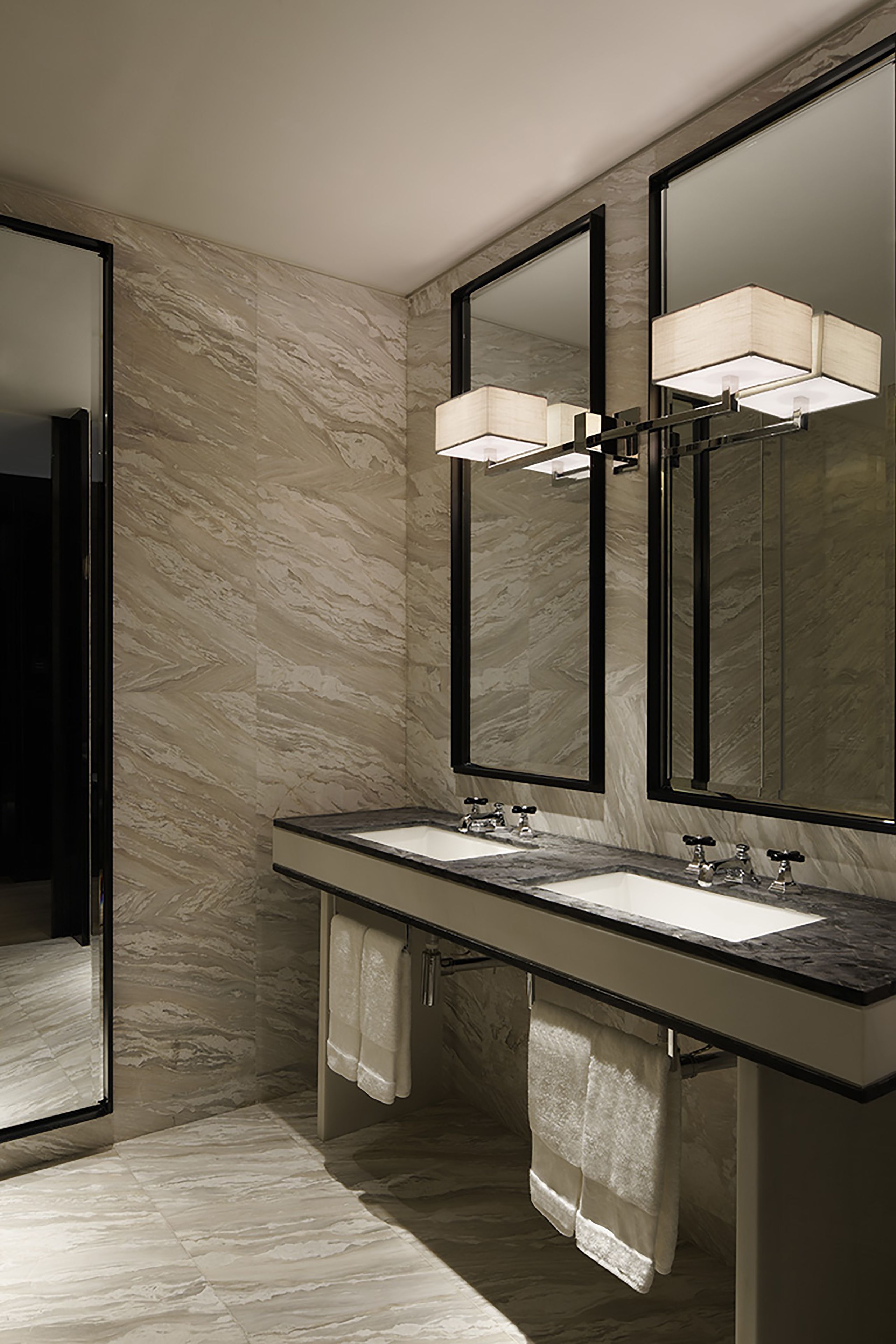 Un baño moderno con dos lavamanos, espejos grandes y piso de mármol.