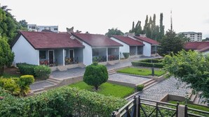 A row of white buildings with red roofs, a paved courtyard, and surrounding greenery. - Rexmar Hotel (Kumasi)