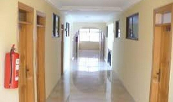 A long, narrow hallway with wooden doors on either side, leading to a bright room at the end. - True Vine Hotel (Kumasi)