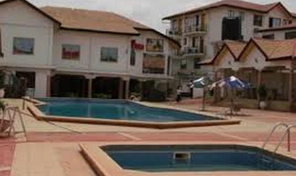 A swimming pool area with adjacent buildings, including a two-story structure with a balcony.