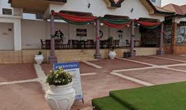 A building with a covered outdoor seating area, a signboard, and potted plants. - True Vine Hotel (Kumasi)