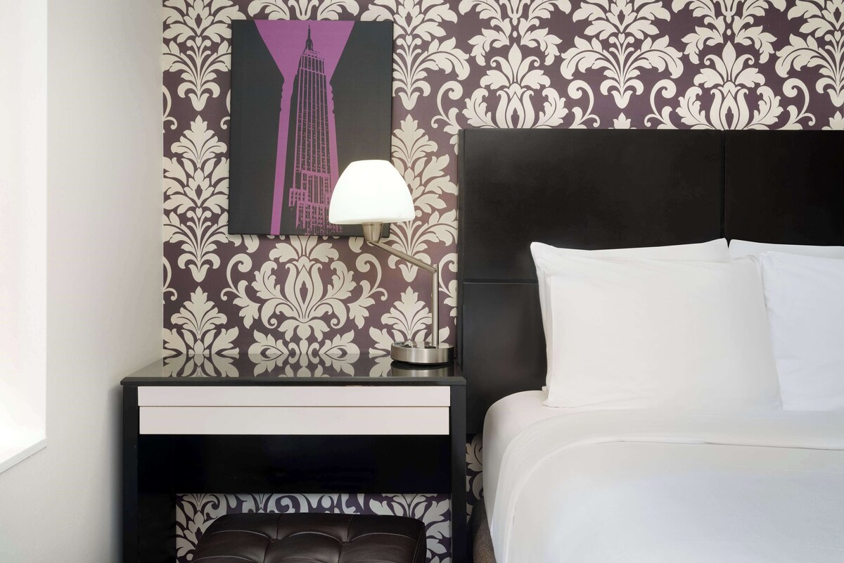 A neatly made bed with white linens, a black headboard, and a bedside table with a lamp.