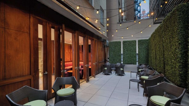 An outdoor seating area with wicker furniture and a green hedge wall. - Best Western Premier Herald Square (New York)