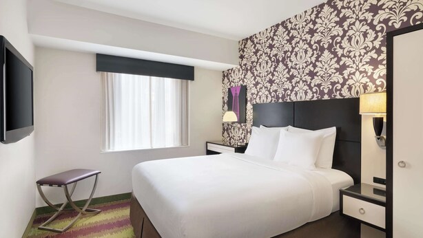 A hotel room with a bed, bedside table, lamp, and a television. - Best Western Premier Herald Square (New York)