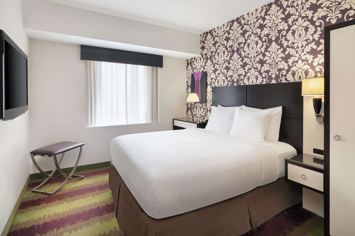 A hotel room with a bed, bedside table, lamp, and a television.