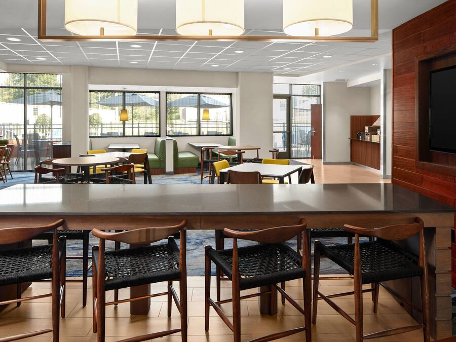 A modern indoor dining area with a central bar, multiple seating options including booths and tables, and large windows providing natural light.