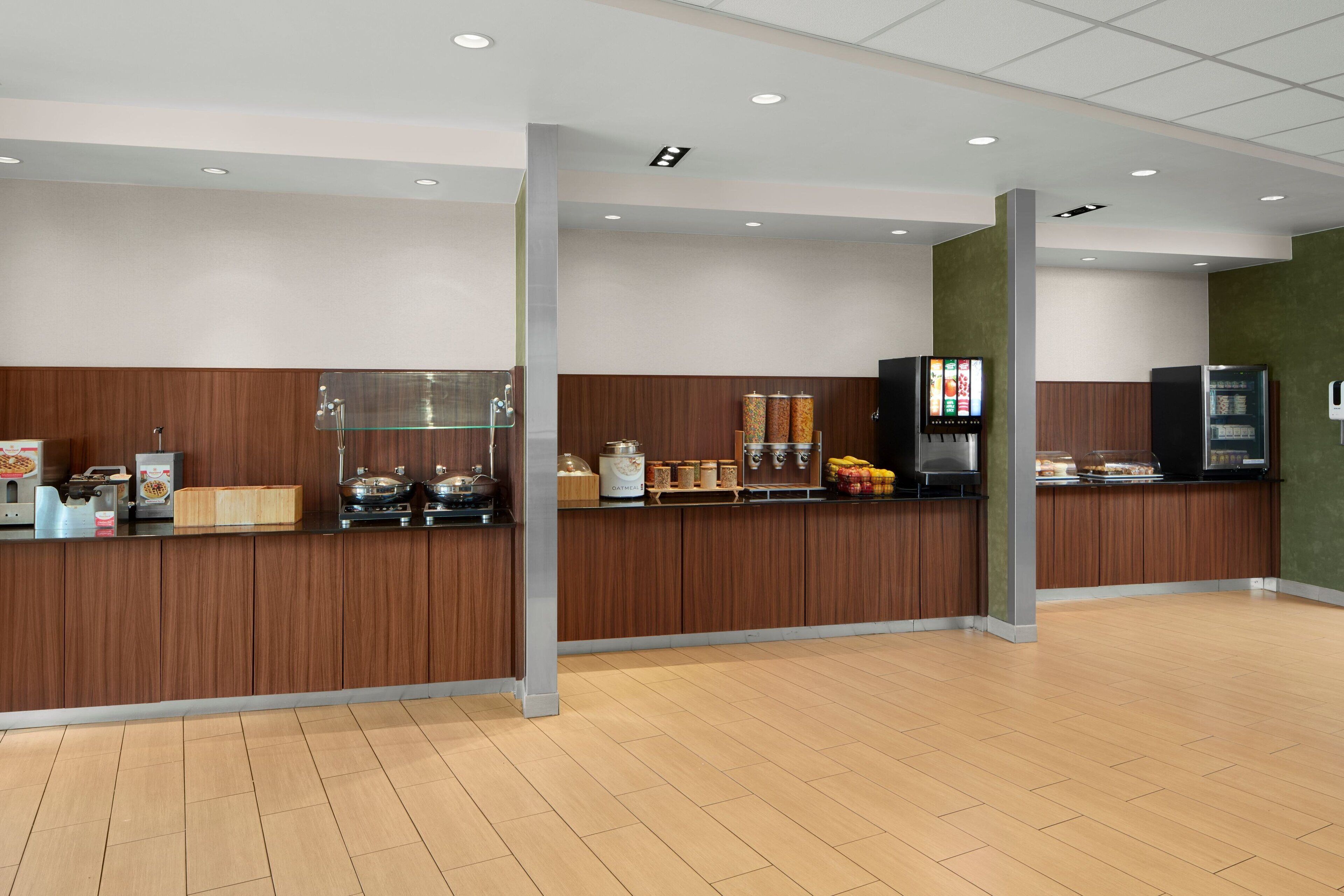 A modern hotel lobby with a wooden reception desk, a coffee machine, and a self-service beverage station.