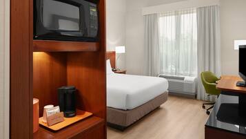 A hotel room with a bed, a desk with a computer, a microwave, a coffee maker, and a window with curtains.