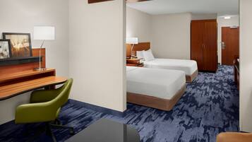 Habitación de hotel con escritorio, dos camas, una silla y piso alfombrado.