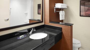 A modern bathroom with a black countertop, a white sink, and a mirror. There is a towel rack with folded towels and a framed picture on the wall.