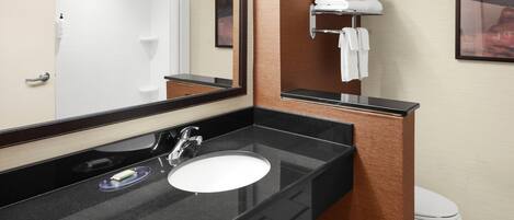 A modern bathroom with a black countertop, a white sink, and a mirror. There is a towel rack with folded towels and a framed picture on the wall.