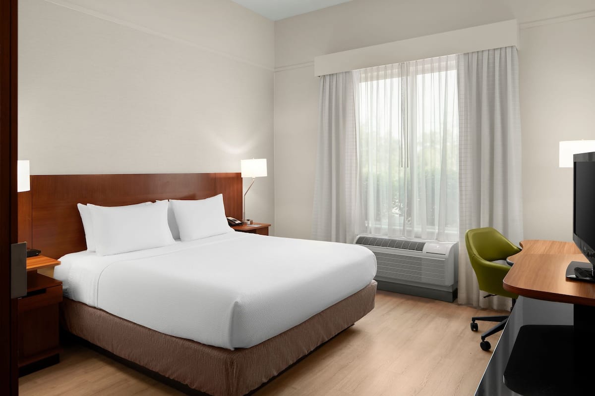 A hotel room with a large bed, a desk with a chair, a television, and a window with curtains.