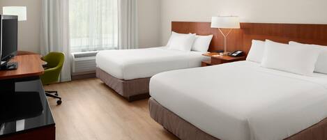 Ein Hotelzimmer mit zwei Betten, einem Schreibtisch mit Computer, einem Stuhl, einer Lampe und einem Fenster mit Vorhängen.