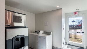 A laundry facility with a front-loading washer and dryer, a vending machine, and an exit sign. - Motel 6 Terrell, TX (Terrell)