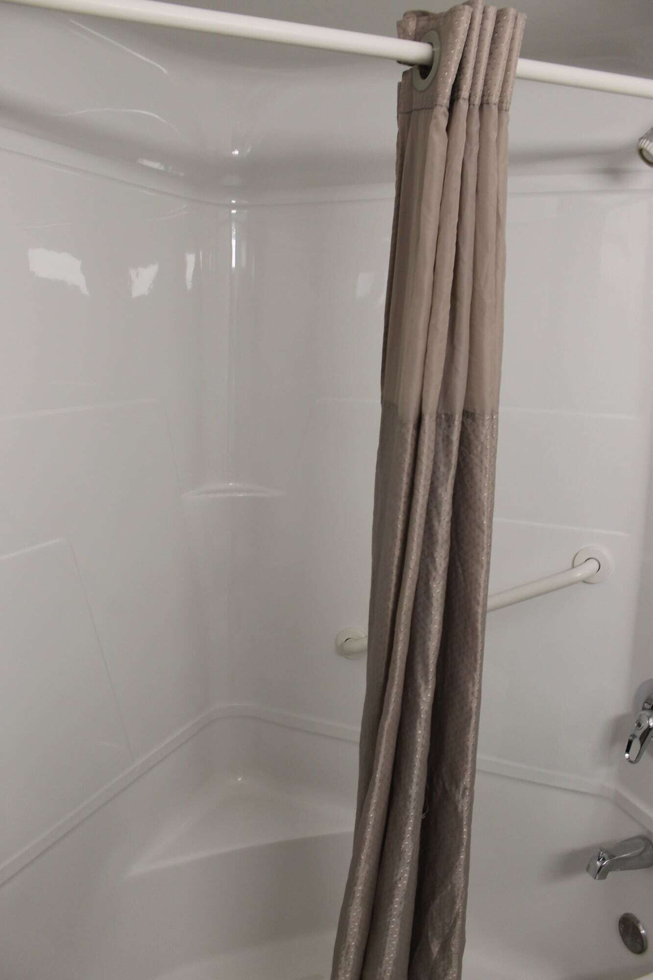 Ein Eckbereich eines Badezimmers mit Duschvorhang, Handtuchhalter und Badewanne.