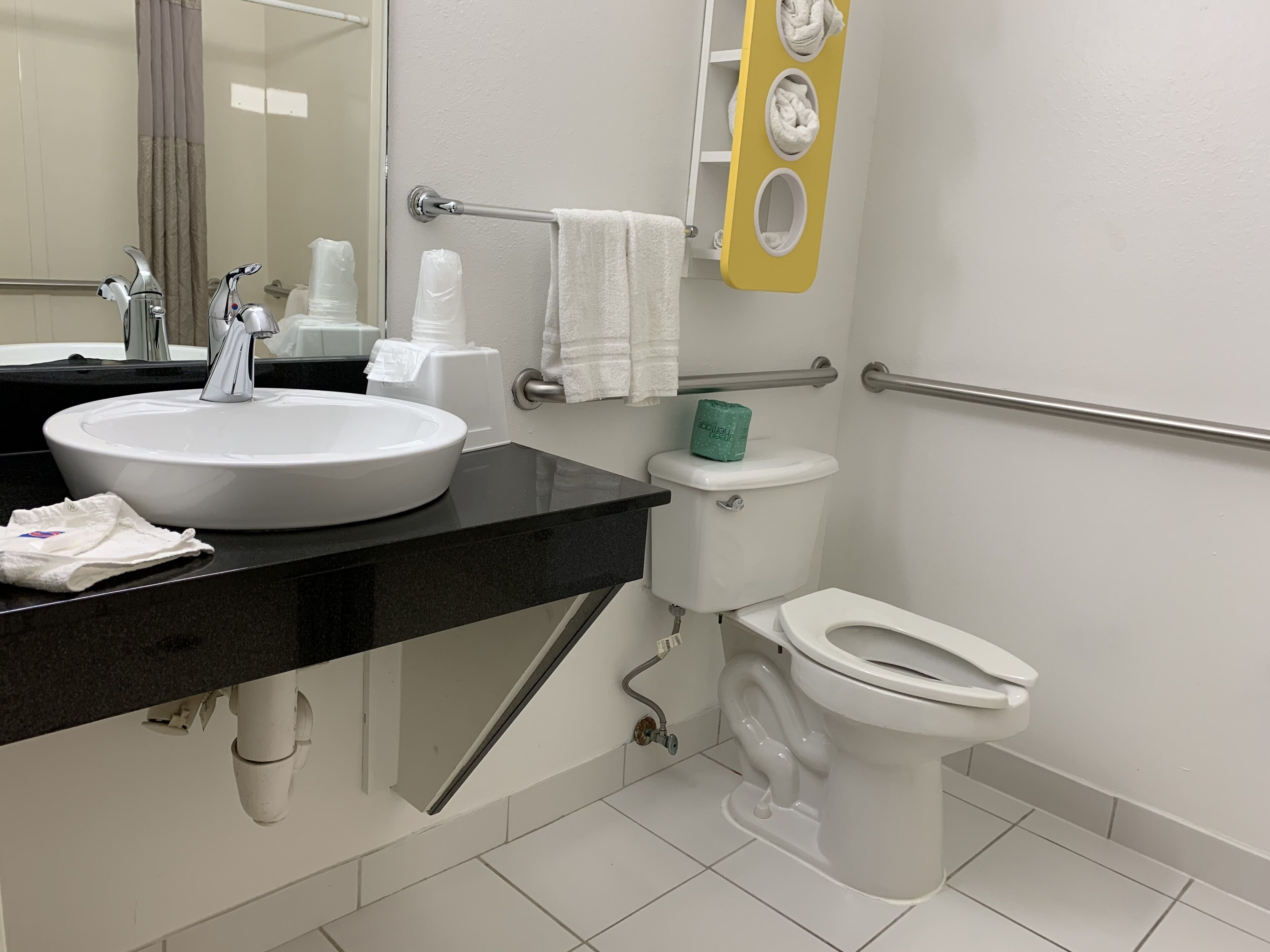 Un baño moderno con un lavabo blanco, encimera negra y un inodoro con toallero amarillo.