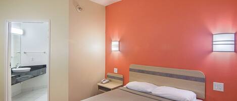 A hotel room with a bed, a nightstand, a phone, and a bathroom visible through an open door.