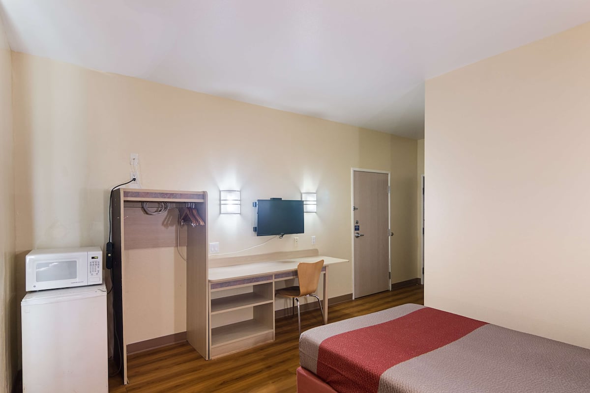 Una habitación de hotel pequeña con cama, escritorio, silla, televisor y microondas.