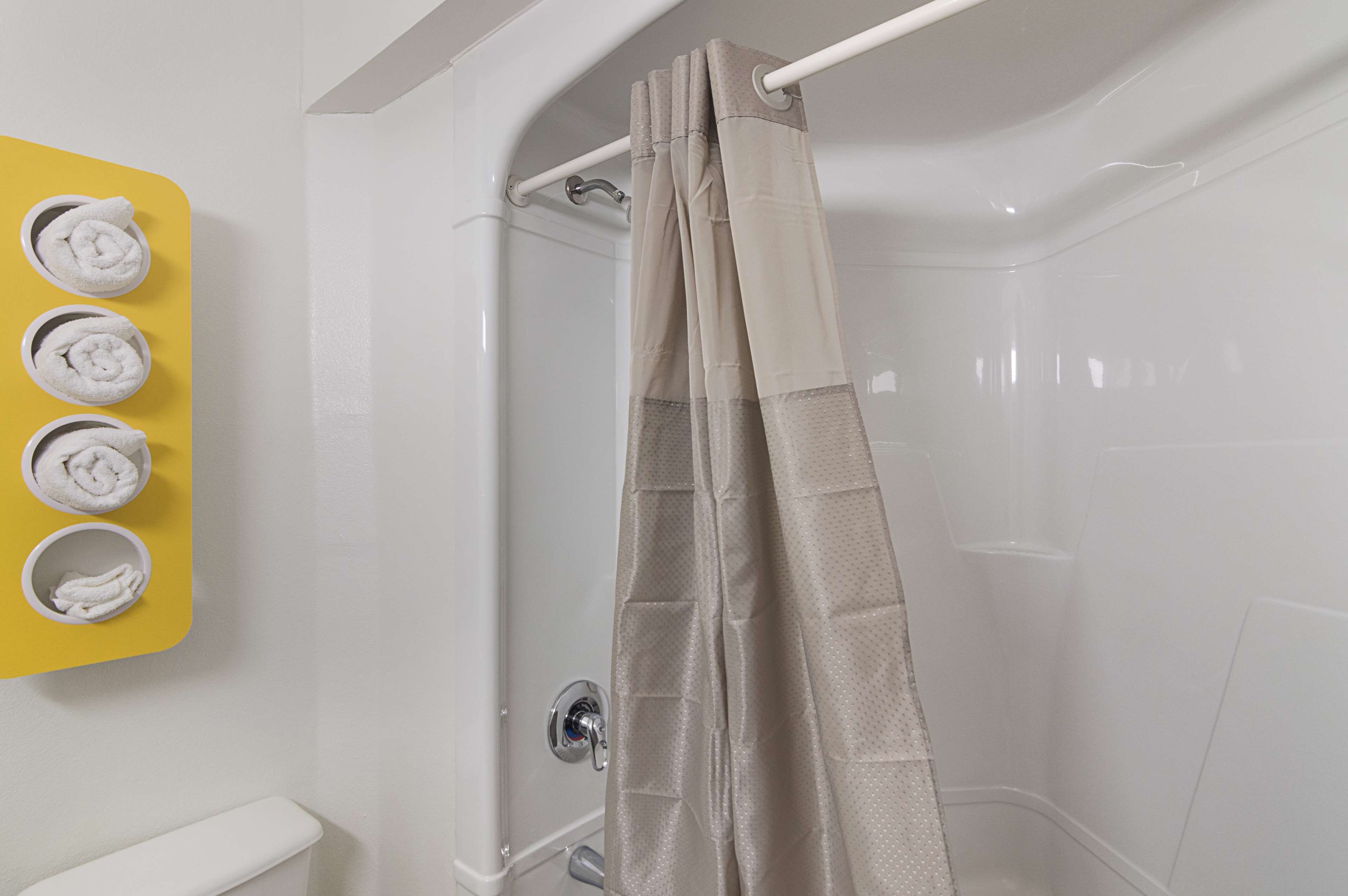 Et bruseområde med et beige bruseforhæng, en hvid væg og en gul håndklædestige med tre håndklæder.