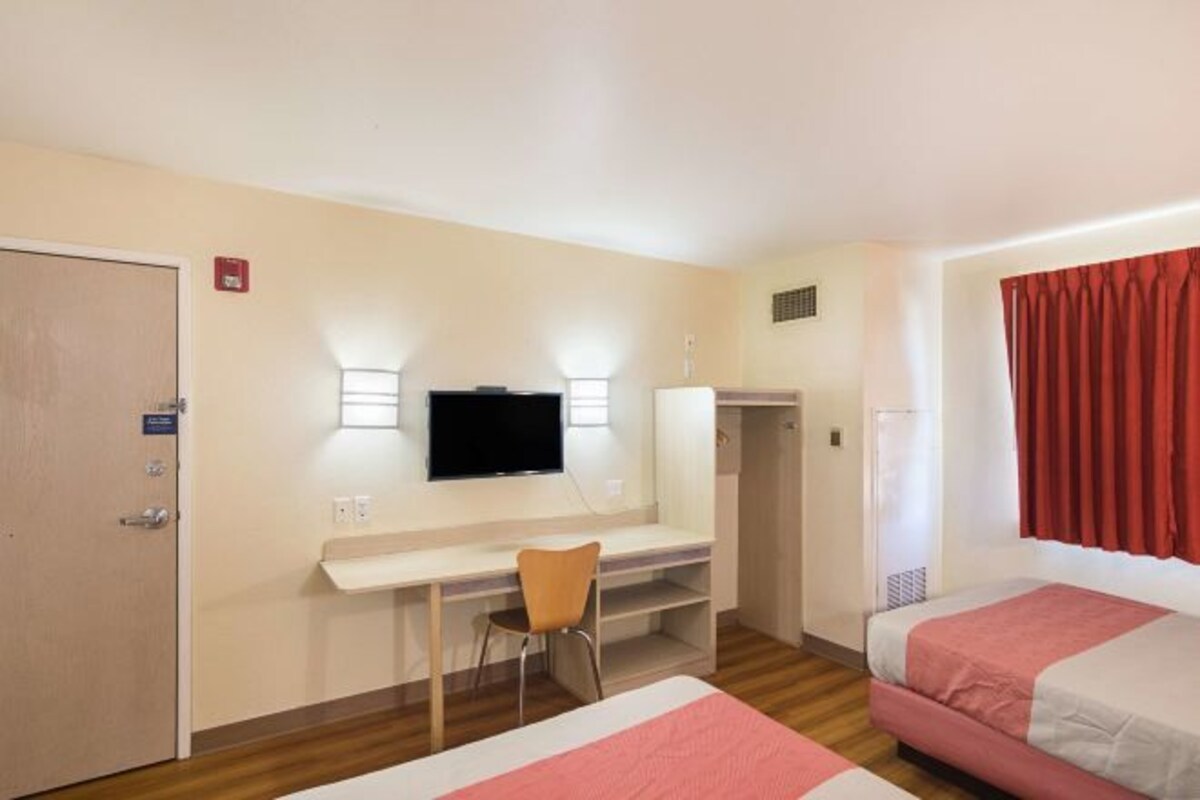 A hotel room with a bed, a desk with a chair, a television, and a wardrobe.