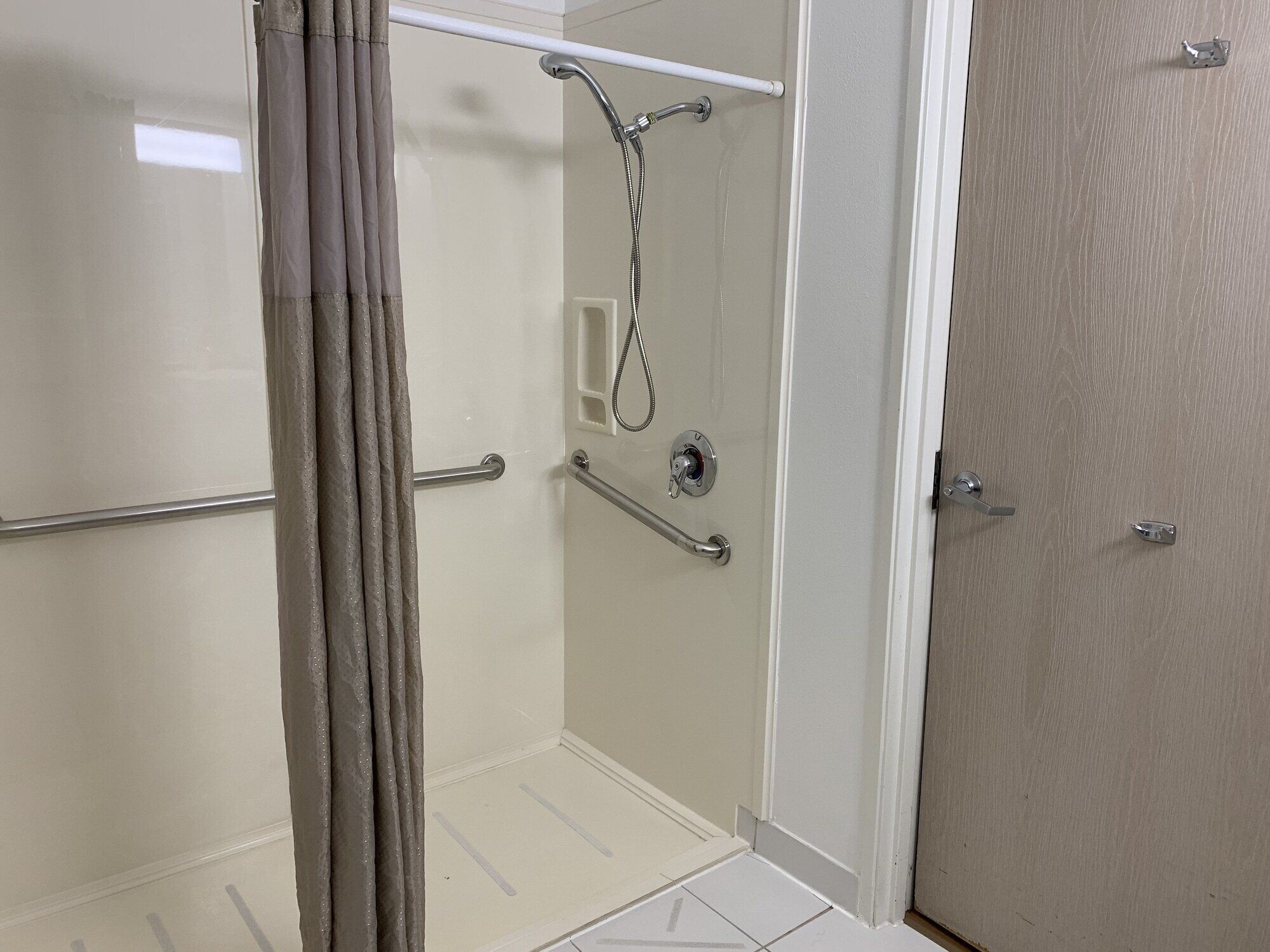 A glass-enclosed shower with a handheld showerhead, grab bars, and a towel rack.