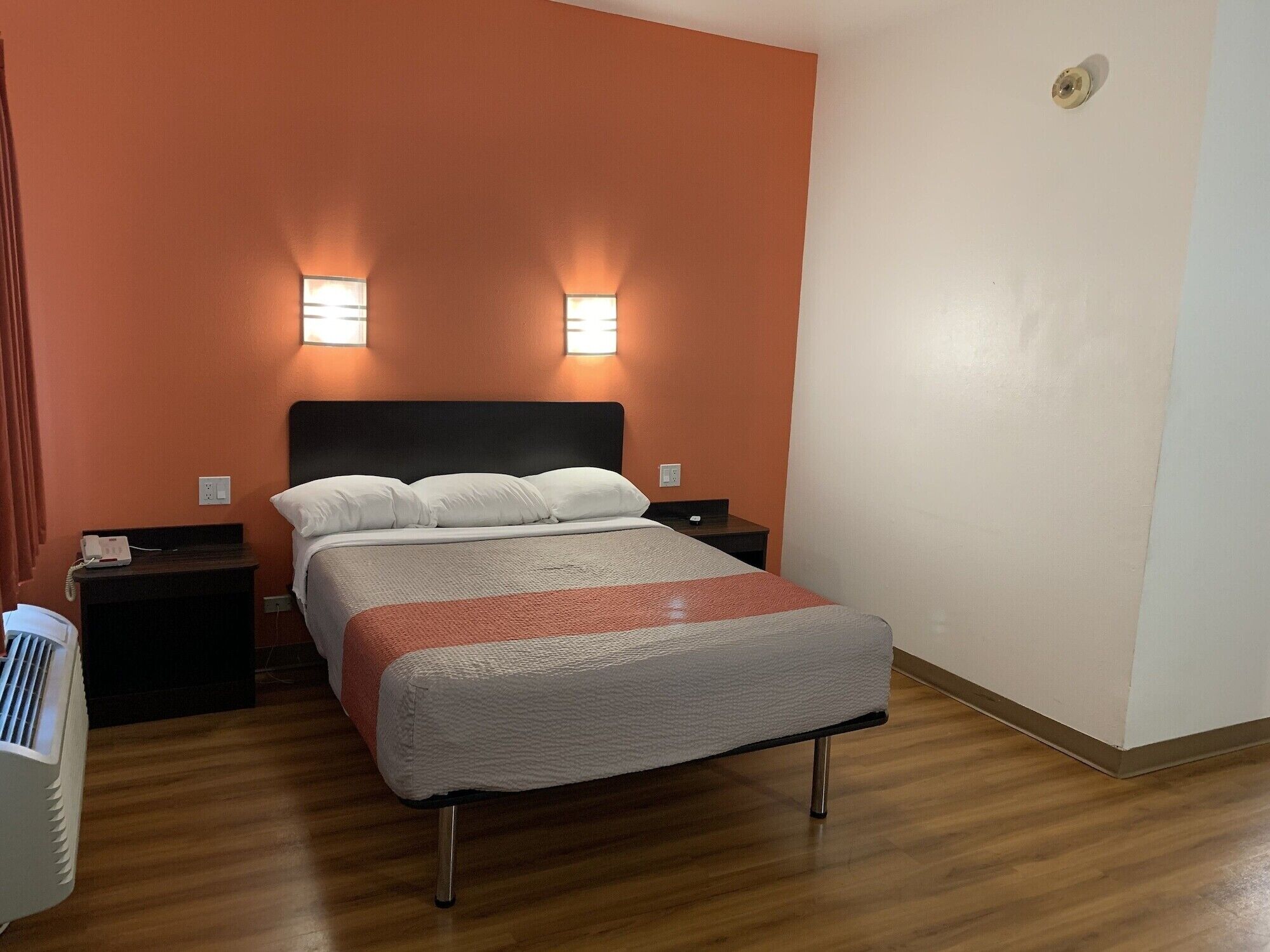 Una habitación de hotel con una cama, dos mesitas de noche y una lámpara de pared.