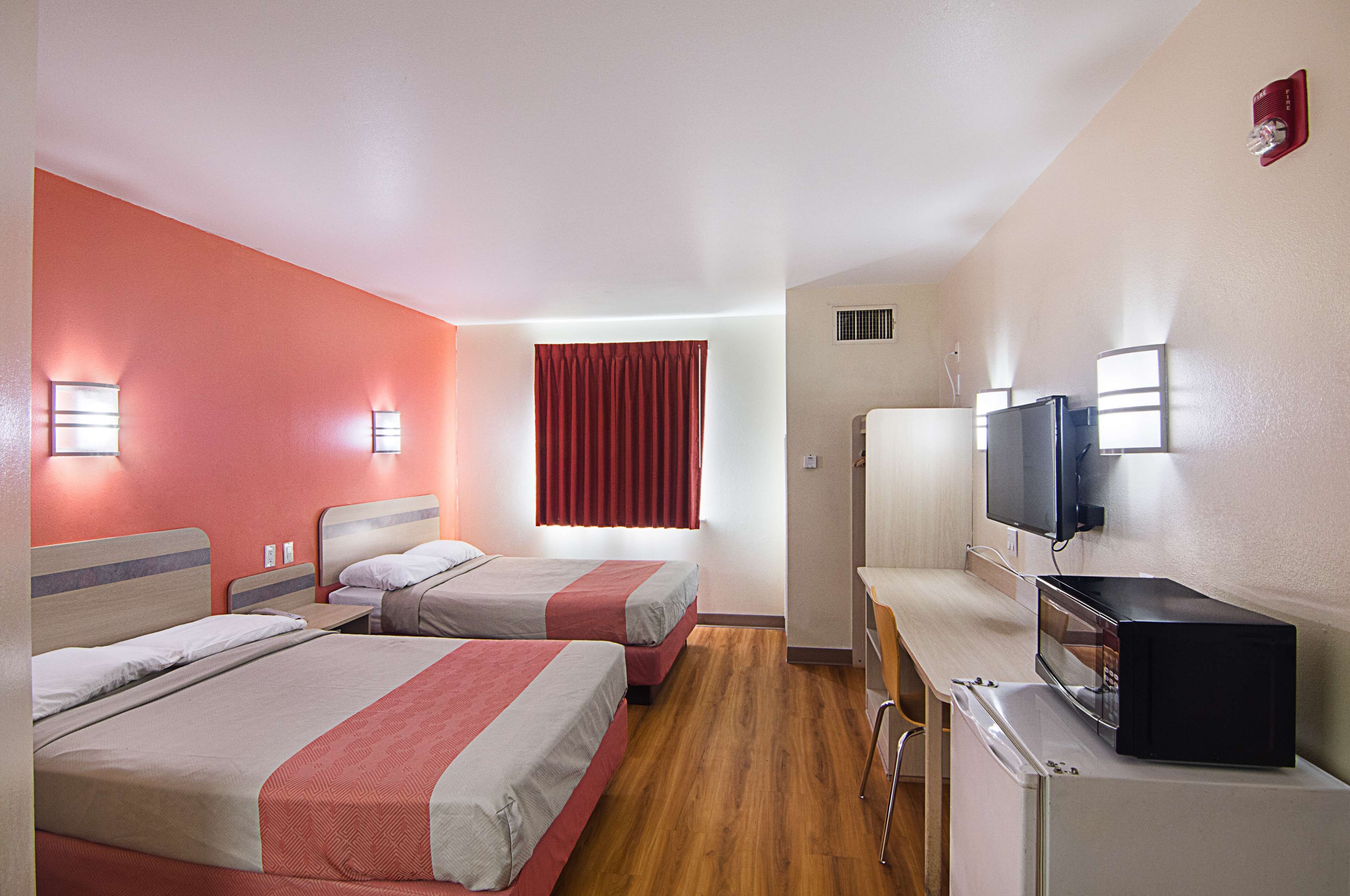 A hotel room with two beds, a desk with a microwave, a TV, and a red curtain.